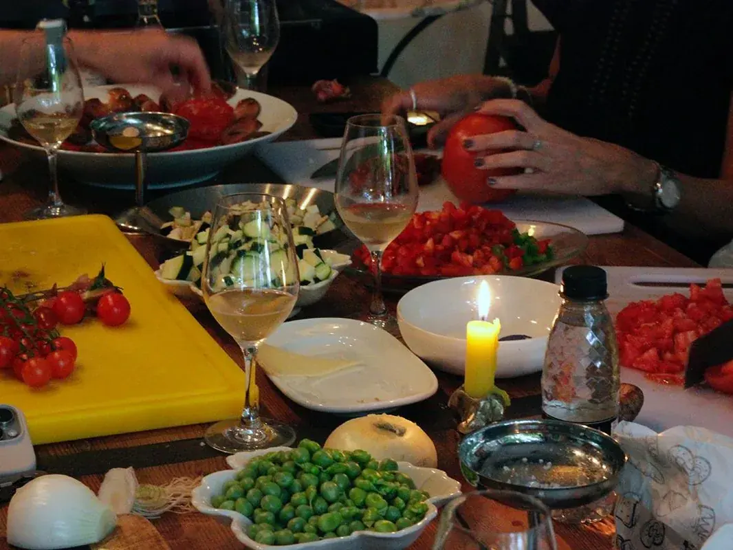 Manos cortando tomate en la mesa de Jugo durante una clase de cocina, con las verduras y las copas de vino alrededor