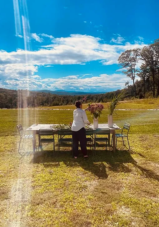 Una mesa puesta en mitad de un prado, con flores, bajo un cielo abierto