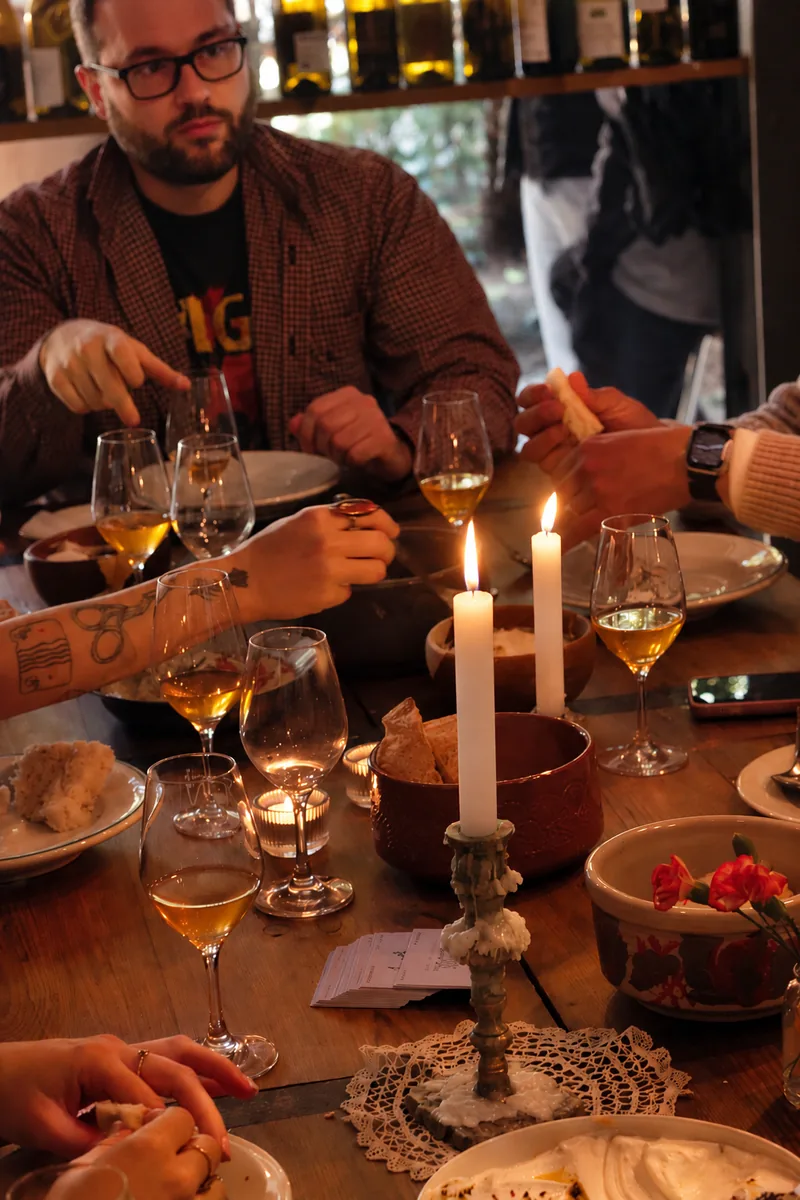 Una mesa de cena en Jugo con velas encendidas, copas de vino y pan, y las manos de los comensales alrededor