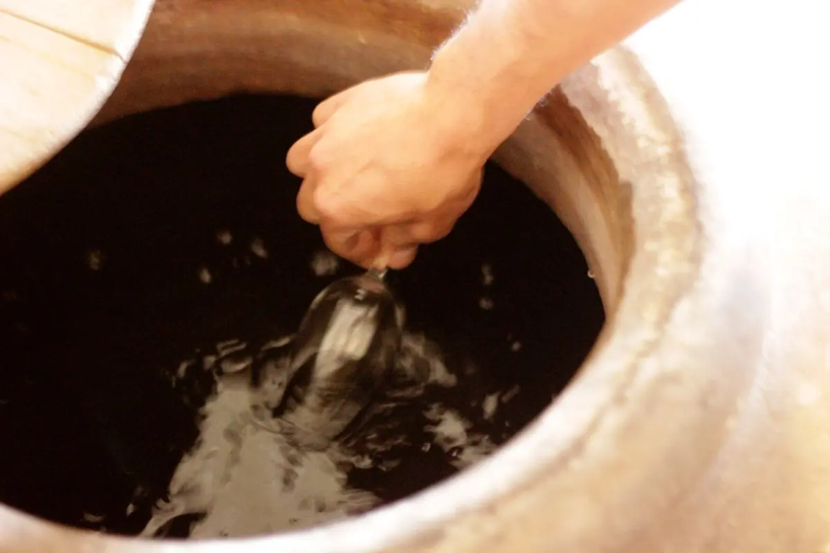Una mano removiendo el vino dentro de una tinaja